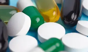 Zbliżenie na białe i zielone kapsułki, żółte i czarne tabletki. Może to być midazolam.