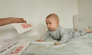Uroczy noworodek na brzuchu, zaciekawiony kartkami z napisami "Mama" i "Tata".