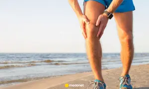 Biegacz na plaży trzyma się za bolące kolano. Może potrzebuje plastrów przeciwbólowych, by wrócić do formy.
