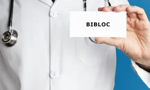 Lekarz w białym kitlu trzyma wizytówkę z napisem BIBLOC. Stetoskop wisi na jego szyi.
