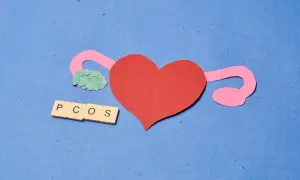 Papierowa grafika przedstawiająca serce, jajniki i litery PCOS na niebieskim tle.