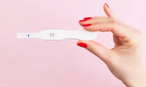 Dłoń z czerwonymi paznokciami trzyma test ciążowy z dwoma kreskami, sugerującymi ciążę biochemiczną.