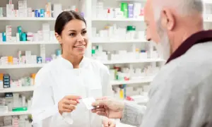 Farmaceutka podaje starszemu panu leki. W tle widać półki pełne opakowań, być może z eliquis.