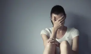 Kobieta siedzi przy ścianie, zakrywając twarz dłońmi. Czasem każdy potrzebuje chwili miansec, by zebrać myśli.