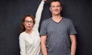 Kobieta z wyrazem zaskoczenia na twarzy mierzy wzrost mężczyzny, przykładając dłoń do jego głowy.