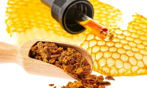 Propolis co to? Złota kropla z pipety na plastrze miodu, obok drewnianej łyżki z pyłkiem.