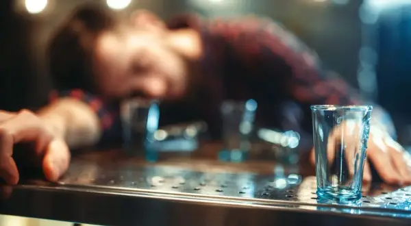 Zasypany alkoholem mężczyzna leży na barze, a obok puste kieliszki. Czy zastanawiasz się, jak szybko wytrzeźwieć?