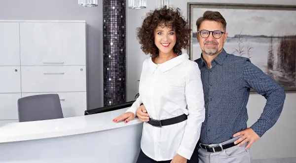 Para uśmiechniętych ludzi w nowoczesnym wnętrzu, prawdopodobnie recepcji medycznej.