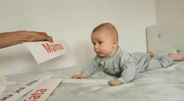 Uroczy noworodek na brzuchu, zaciekawiony kartkami z napisami "Mama" i "Tata".