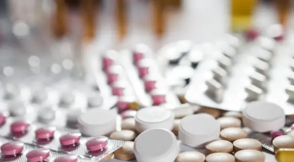 Zbliżenie na opakowania leków i tabletki, w tym różowe tabletki w blistrze i białe tabletki luzem. Może to być lek pramolan 50 mg.