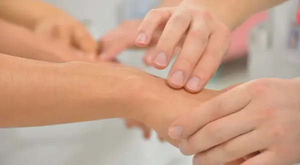Dłoń lekarza bada nadgarstek pacjenta, oceniając drżenie rąk.