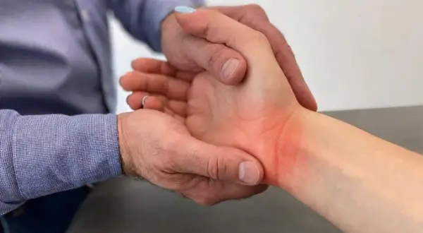 Fizjoterapeuta bada zaczerwieniony nadgarstek pacjenta, delikatnie go dotykając.