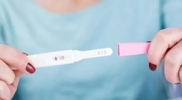 Dłoń trzyma test ciążowy z widocznym jednym paskiem. Rozważana jest opcja przerwania ciąży, być może z użyciem mizoprostolu.
