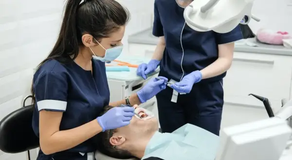 Dwie dentystki w maseczkach i rękawiczkach wykonują zabieg u pacjenta.