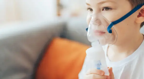 Chłopiec w masce inhalatora z niebieską opaską, wykonujący inhalację.