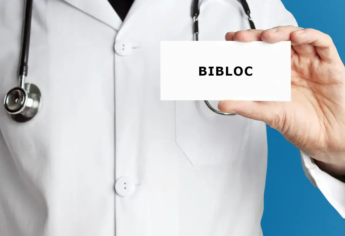 Lekarz w białym kitlu trzyma wizytówkę z napisem BIBLOC. Stetoskop wisi na jego szyi.