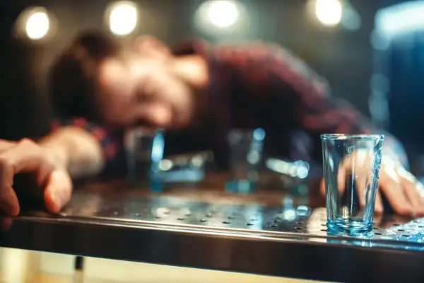 Zasypany alkoholem mężczyzna leży na barze, a obok puste kieliszki. Czy zastanawiasz się, jak szybko wytrzeźwieć?