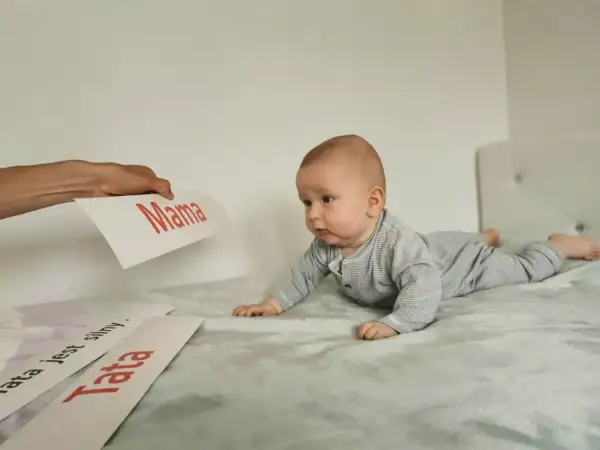 Uroczy noworodek na brzuchu, zaciekawiony kartkami z napisami "Mama" i "Tata".