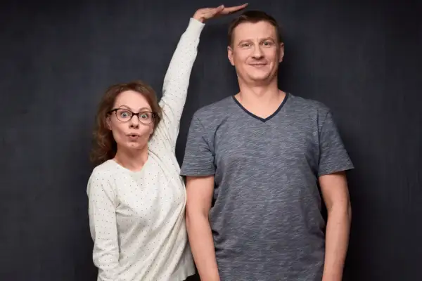 Kobieta z wyrazem zaskoczenia na twarzy mierzy wzrost mężczyzny, przykładając dłoń do jego głowy.